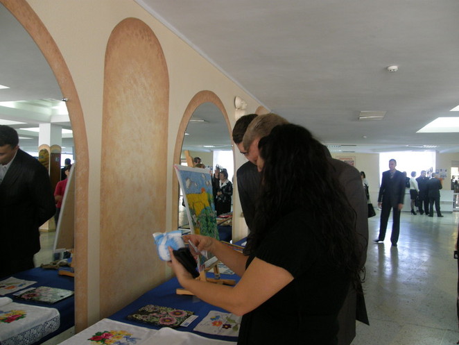 Н. Круглову показывают один из интереснейших экспонатов выставки - "бело-голубую" елочную игрушку со стишком о президенте