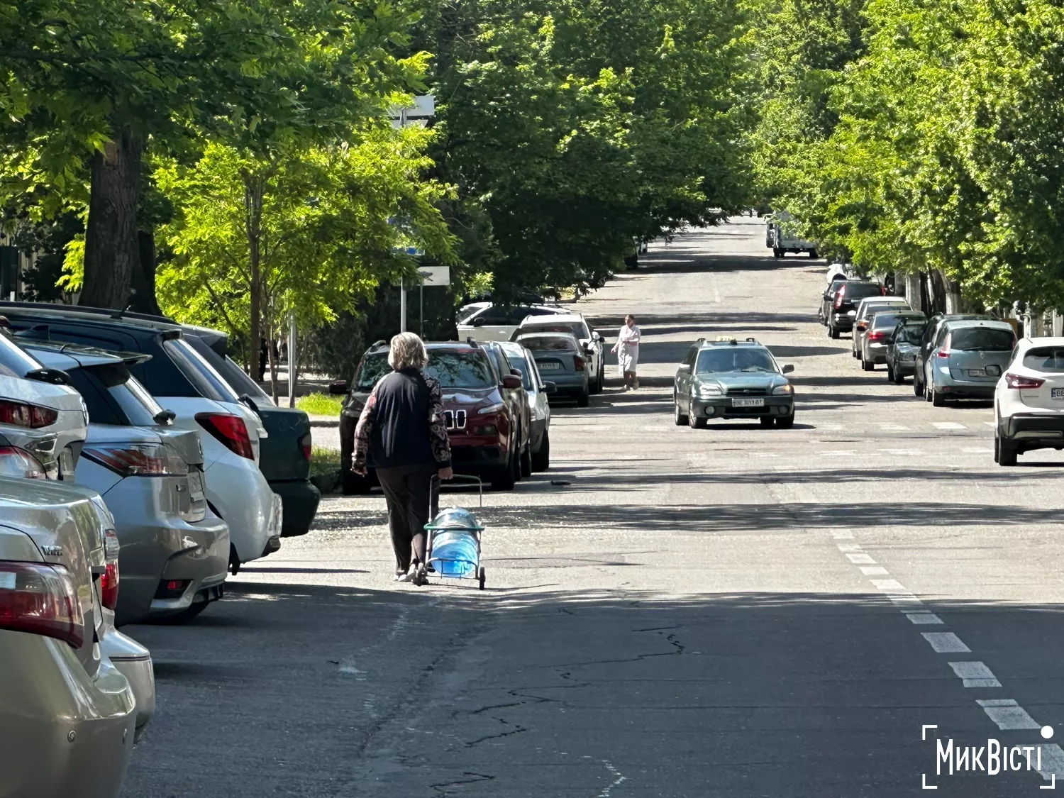 Жінка тягне кравчучкою 18-літрову баклажку з водою у центрі Миколаєві, травень 2025 року. Фото «НикВести»